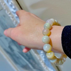 May include: A bracelet made of iridescent white and yellow beads. The beads are round and have a smooth, polished finish.