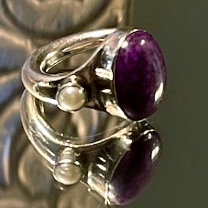 Peut inclure: Une bague en argent avec une grande pierre précieuse violette et un petit accent de perle.