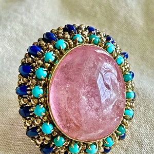 May include: A pink gemstone ring with a gold setting and a halo of blue and turquoise stones.