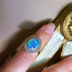 May include: A silver ring with a large oval opal gemstone surrounded by a halo of smaller clear gemstones.