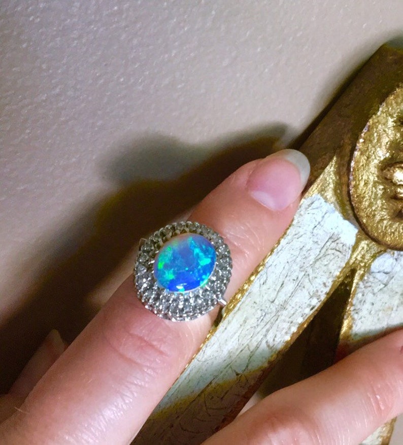 May include: A silver ring with a large oval opal gemstone surrounded by a halo of smaller clear gemstones.