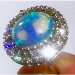 May include: A silver ring with a large oval opal gemstone. The opal is a light blue color with flashes of green and white.