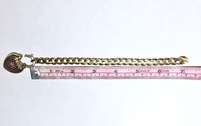 May include: A gold chain bracelet with a heart-shaped charm encrusted with red rhinestones. The bracelet measures 7 inches long.