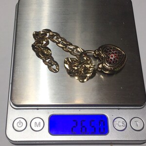 May include: A gold chain necklace with a heart-shaped pendant encrusted with red gemstones. The necklace is on a digital scale that reads 26.50.