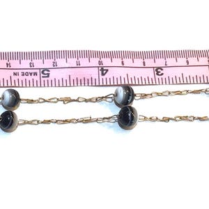 May include: A vintage necklace featuring alternating black and white striped beads strung on a delicate gold-tone chain. The necklace is shown with a pink measuring tape.