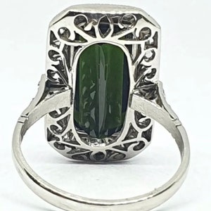 May include: A silver ring featuring a large, rectangular, dark green gemstone. The gemstone is set within an ornate, filigree-style frame. The ring band is a simple, polished silver.