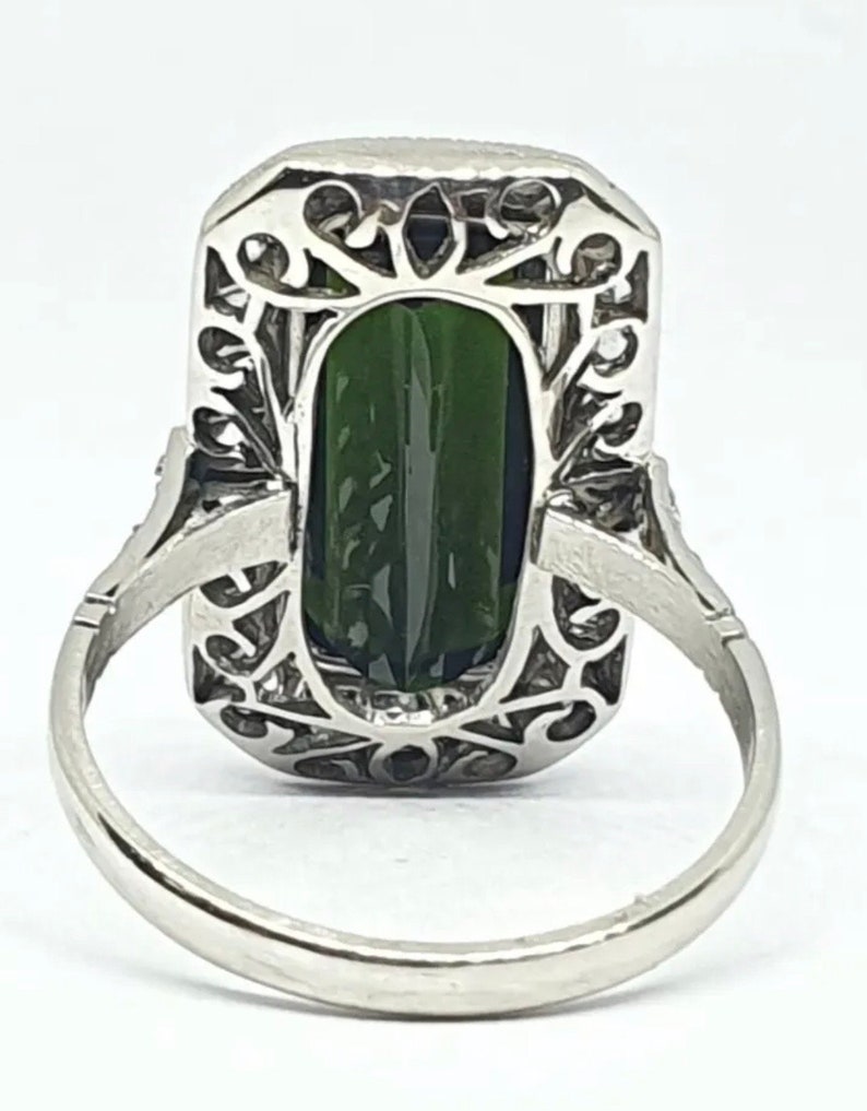 May include: A silver ring featuring a large, rectangular, dark green gemstone. The gemstone is set within an ornate, filigree-style frame. The ring band is a simple, polished silver.