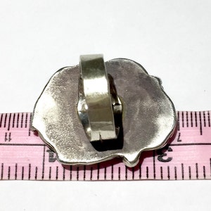 以下が含まれることがあります： テクスチャ加工が施された不規則な形のデザインのシルバーリング。リングはピンクの定規で測定されています。