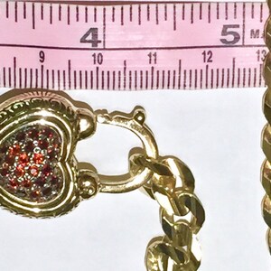 May include: A gold heart-shaped locket with a red rhinestone design, attached to a gold curb chain.