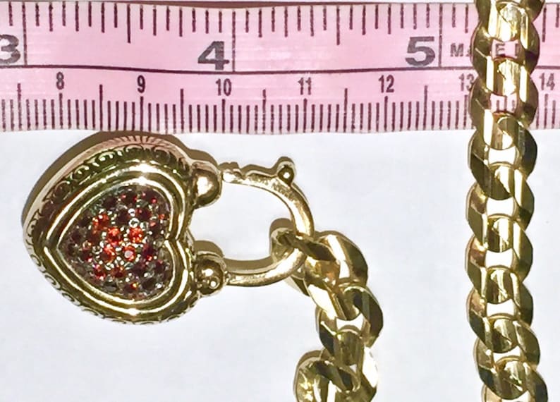 May include: A gold heart-shaped locket with a red rhinestone design, attached to a gold curb chain.