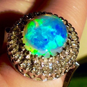 May include: A silver ring with a large, round, iridescent opal gemstone surrounded by a halo of smaller, clear gemstones.