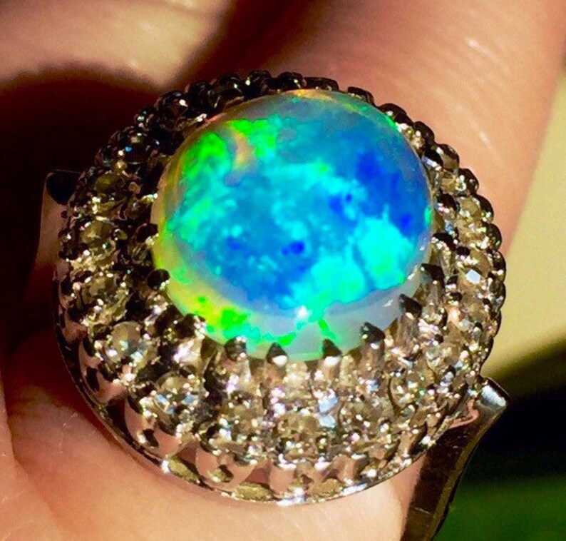 May include: A silver ring with a large, round, iridescent opal gemstone surrounded by a halo of smaller, clear gemstones.
