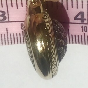 May include: A gold-colored pendant with a black stone set in a heart-shaped design. The pendant is approximately 1 inch in diameter.