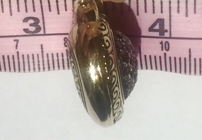 May include: A gold-colored pendant with a black stone set in a heart-shaped design. The pendant is approximately 1 inch in diameter.