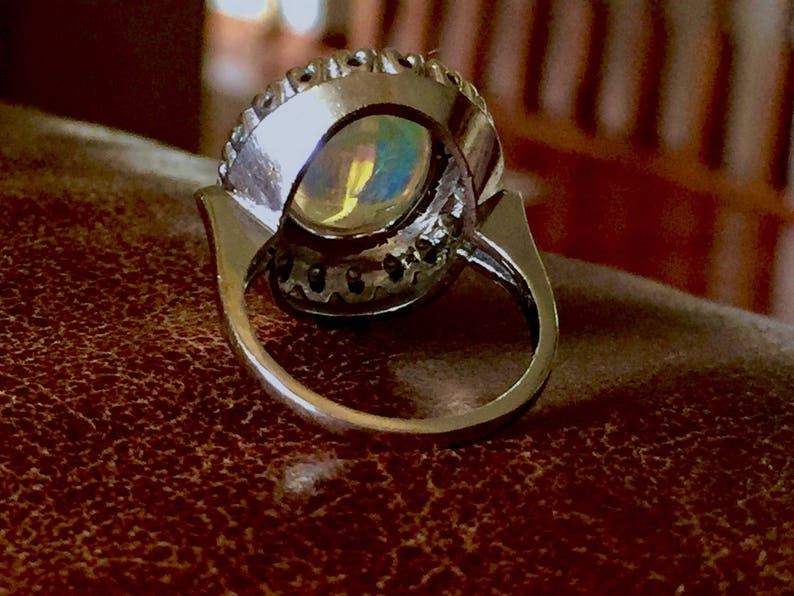 May include: A silver ring with a large oval opal gemstone surrounded by a halo of smaller diamonds.
