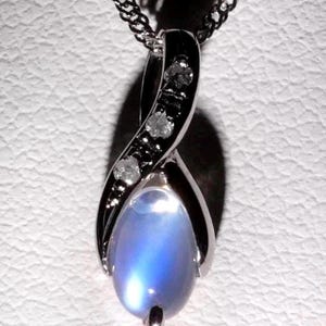 May include: A silver pendant necklace featuring a pear-shaped, iridescent blue gemstone. The pendant has a twisted design with small, clear accent stones. The necklace chain is a delicate silver.