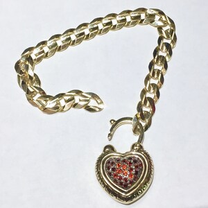 May include: A gold chain bracelet with a heart-shaped padlock charm. The padlock is decorated with red and clear gemstones.