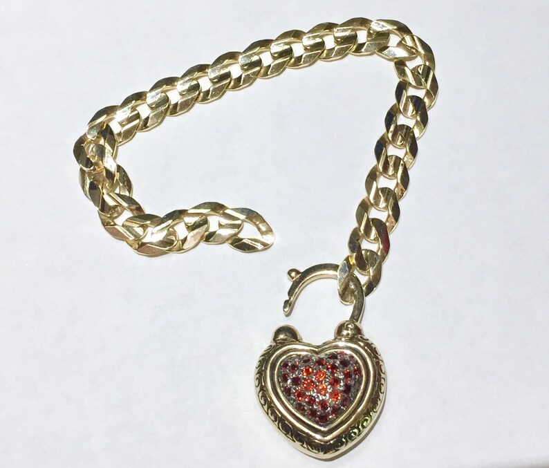 May include: A gold chain bracelet with a heart-shaped padlock charm. The padlock is decorated with red and clear gemstones.