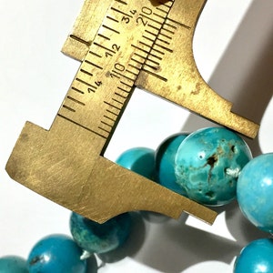 Puede incluir: Primer plano de un collar de cuentas turquesa con una regla que mide el tama&ntilde;o de una de las cuentas. La cuenta tiene aproximadamente 1,2 cm de di&aacute;metro.