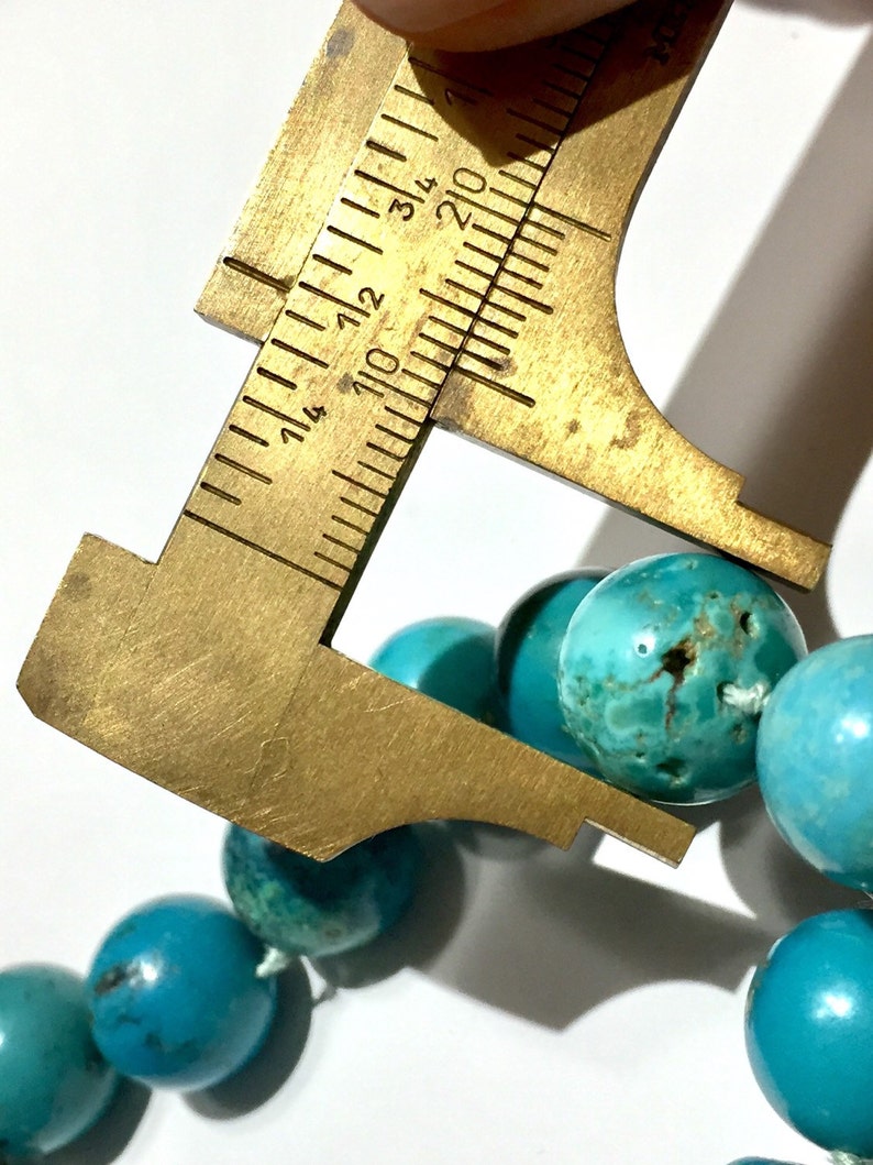 Puede incluir: Primer plano de un collar de cuentas turquesa con una regla que mide el tama&ntilde;o de una de las cuentas. La cuenta tiene aproximadamente 1,2 cm de di&aacute;metro.