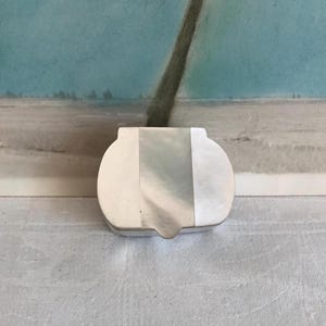 May include: A set of three ceramic mugs with a speckled, matte finish. The mugs are in shades of cream, light brown, and dark brown. Each mug has a simple, minimalist design, perfect for coffee or tea.