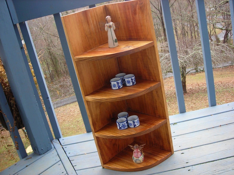 Peut inclure: Une &eacute;tag&egrave;re d'angle en bois avec trois &eacute;tag&egrave;res. Les &eacute;tag&egrave;res sont incurv&eacute;es et ont une teinte brun clair. Il y a de petites tasses en c&eacute;ramique bleu et blanc sur les &eacute;tag&egrave;res, et une petite figurine d'ange en bois sur l'&eacute;tag&egrave;re sup&eacute;rieure.