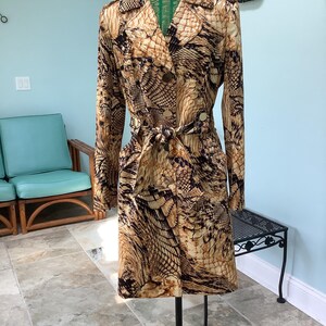 May include: A vintage trench coat with a snakeskin pattern in shades of brown, tan, and black. The coat features a double-breasted closure, a matching belt, and long sleeves. The coat is displayed on a mannequin.