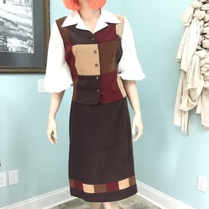 May include: A vintage two-piece outfit on a mannequin. The ensemble includes a white blouse with wide sleeves, a patchwork vest in shades of brown and burgundy, and a matching brown skirt with a patchwork hem. The outfit is a retro style.