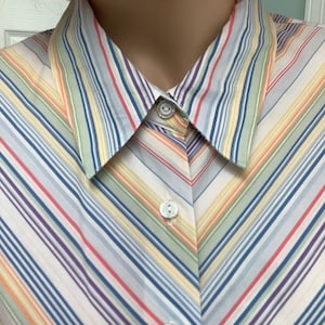 May include: A button-down shirt with a colorful striped pattern in shades of blue, green, yellow, orange, and purple. The shirt has a pointed collar and three decorative buttons. The stripes run diagonally across the fabric.