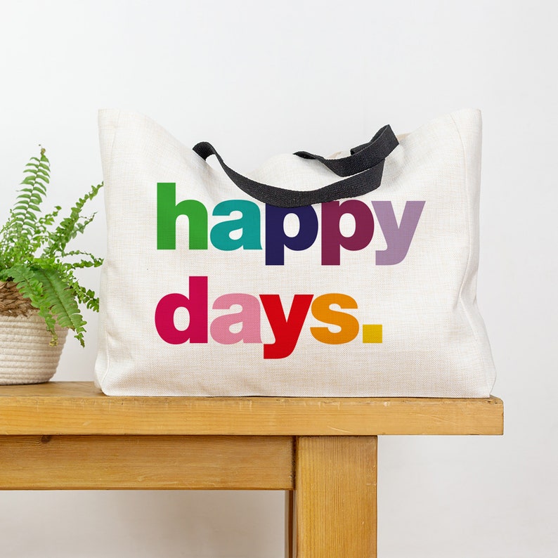 May include: A white canvas tote bag with black handles and the text "happy days." printed in rainbow colours.