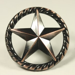May include: A copper and silver five-pointed star with a rope-like border. The star is in a circle.
