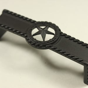 May include: Black metal cabinet pull with a rope design and a star cutout in the center.