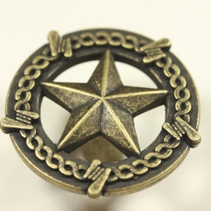 May include: A gold-toned metal knob with a five-pointed star design surrounded by a barbed wire rope design.