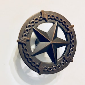 May include: Bronze-colored cabinet knob featuring a five-pointed star within a circular frame. The frame has a rope-like design with decorative elements. The knob is likely made of metal and has a rustic, vintage aesthetic.