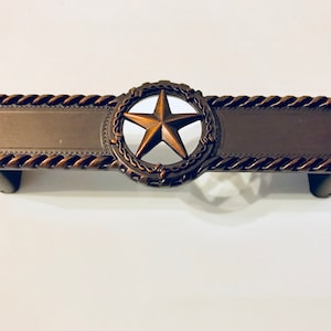 May include: A bronze cabinet pull with a rope design border and a five-pointed star in a barbed wire circle.