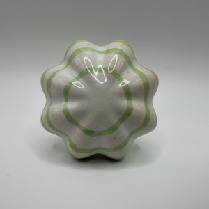 May include: A white ceramic knob with green stripes. The knob is shaped like a flower with six petals.