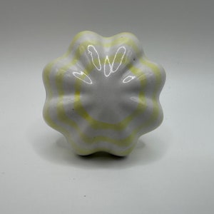May include: A white ceramic knob with yellow stripes. The knob is shaped like a flower with five petals.