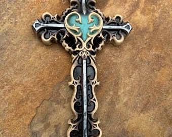 May include: A decorative wooden cross with a teal heart in the center. The cross is intricately carved with a black and silver finish.