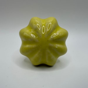 May include: A yellow ceramic knob with a starburst design. The knob has a smooth, glossy finish.
