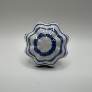 May include: A white ceramic knob with blue stripes. The knob is shaped like a flower with six petals.