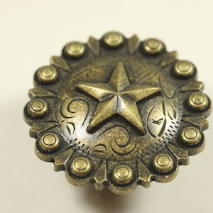 May include: A gold-toned metal star-shaped button with a decorative border of small circles. The button has a rustic, antique look.
