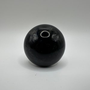 May include: A smooth, black obsidian sphere with a slight sheen. The sphere is perfectly round and has a polished finish.
