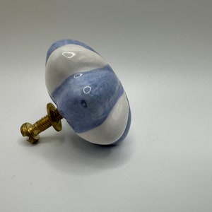 May include: A blue and white ceramic knob with a swirl pattern. The knob has a brass screw.