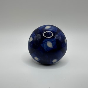 May include: A blue and white ceramic sphere with a speckled pattern. The sphere is smooth and round.