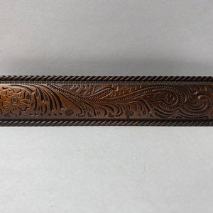 May include: A brown metal rectangular drawer pull with a rope-like border and an embossed floral design.