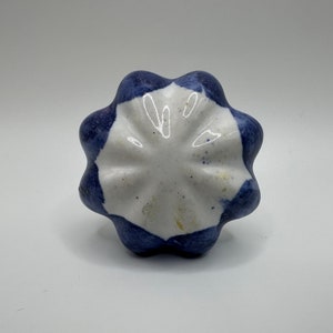 May include: A white ceramic knob with a blue and white geometric pattern. The knob has a scalloped edge and a slightly raised center.