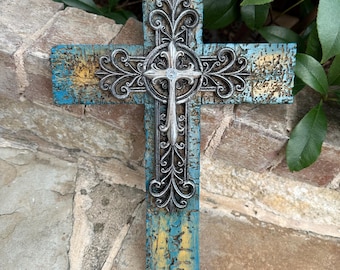 May include: A rustic wooden cross with a distressed blue and yellow paint finish. The cross features a silver metal design with intricate details.