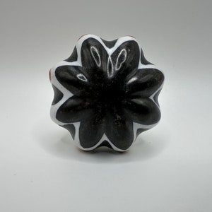 May include: Black and white ceramic knob with a flower-like design. The knob has a raised center and six points.