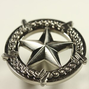 May include: Silver-toned metal star-shaped knob with a decorative border. The star is raised and has a brushed finish. The border is a chain-like design.