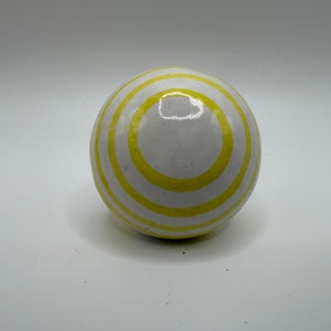 May include: A white ceramic sphere with yellow stripes. The sphere has a glossy finish.